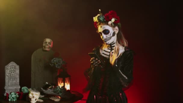 黒の背景にインターネットのウェブサイトを閲覧するためにスマートフォンを使用してグラマラスな怖い女性 Santa Muerte Model Portraying Horror Goddess Death Mexican Holiday — ストック動画