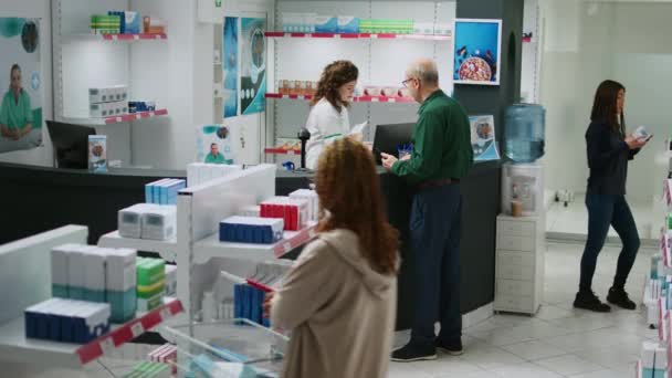 高齢のクライアントは 処方治療のための薬について薬剤師に尋ねる 薬の製品や薬のボトルを購入しようとして 薬局で医療病の老人 — ストック動画