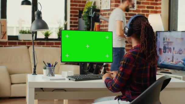 使用绿色屏幕和耳机听音乐的非裔美国人 使用带有彩色键显示和独立模拟的计算机 看着空白的绿色屏幕 三脚架射击 — 图库视频影像