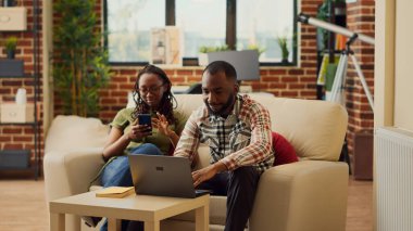 Kız arkadaş ve erkek arkadaş akıllı telefon ve dizüstü bilgisayara bakıyorlar, internet ağında boş zamanların tadını çıkarıyorlar. Çiftler modern aletleri kullanırken eğleniyor ve gülümsüyorlar..