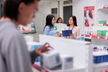 Reçeteli ilaçlardan bahseden Asyalı kadınlar takımı, müşterilerine ilaç takviyeleri hakkında tıbbi tavsiyelerde bulunan danışman. Müşteri ve işçi ilaç paketini analiz ediyor.