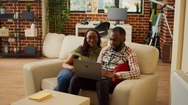 Erkek arkadaş ve kız arkadaş dizüstü bilgisayarda videolar izliyor, kanepede birlikte rahatlıyor ve eğleniyorlar. İnternette gezinmek, boş zamanların tadını çıkarmak, evde oturarak gülmek..