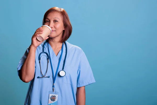 Zmęczona Pielęgniarka Niebieskim Mundurze Stetoskopie Pijąca Kawę Przed Kamerą Pracująca — Zdjęcie stockowe