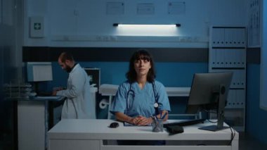 Gülümseyen doktor asistanı masada duruyor. Hastalık belirtilerini kontrol ediyor. Bilgisayarda yazılan sağlık tedavisinde. Muayene sırasında hastane ofisinde çalışan tıbbi asistan.