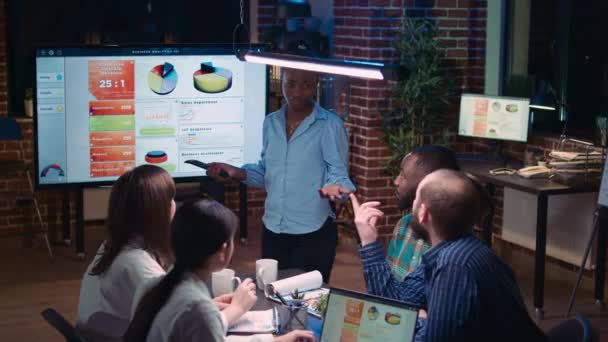 ビジネス分析会議 企業プレゼンテーションを示すアフリカ系アメリカ人のプロジェクトマネージャー 統計について議論するチーム 販売戦略を計画する デジタルボードで図を見る同僚 — ストック動画