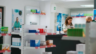 Raflardaki ilaçlara bakan çeşitli müşteriler, reçeteli tedavi veya vitamin almak için halthcare ürünlerini kontrol ediyorlar. Eczanedeki insanlar destek paketlerini inceliyor. Üçayak atışı.