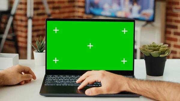 デスクで緑のスクリーンテンプレートを使用してノートパソコンで作業している男性フリーランスは 空白のクロマキーとポータブルコンピュータ上の隔離されたディスプレイを確認します コピースペースをモックアップしたPcを見てください 三脚が撃たれた 閉じろ — ストック写真