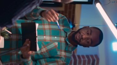 Dikey video: Afro-amerikan işletme koçu şirket toplantısında sunum yapıyor, pano tutuyor, rapor okuyor. Analitik araştırma çizelgeleri, gece vakti istatistikleri gösteren bir çalışan