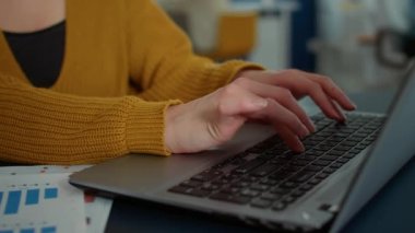 Dizüstü bilgisayarda yazan kadın ellerine yakın çekim ve başlangıç ofisindeki masada oturan kameraya gülümseme. İş yerinde taşınabilir bilgisayarla rahatça çalışan sıradan bir çalışanın portresi.