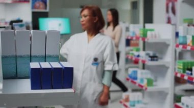 Eczacı eczane raflarındaki kardiyoloji haplarına bakıyor, eczanede tıbbi ürünlerle çalışıyor. Eczacılık işçisi eczane perakende mağazasında kutu kutu ilaç okuyor..