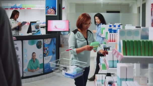 薬局の棚にビタミンの箱を読んでいる女性の顧客は 医薬品のパッケージを見て ドラッグストアで処方薬や治療を探しているアジア人 — ストック動画