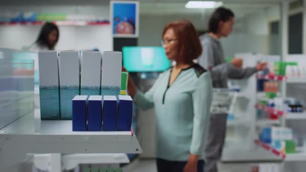 薬局で薬を探しているアジアの女性は 薬箱やボトルでいっぱいの棚を見ています ドラッグストアのクライアント読書薬パッケージ 医薬品 — ストック動画