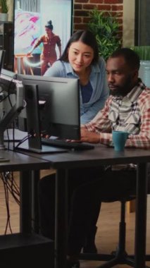 Dikey video: Yaratıcı ajans stüdyosunda çalışan çok ırklı çalışanlardan oluşan bir ekip profesyonel yazılım üzerinde 3D içerik geliştiriyor. Sanatsal becerilerle bilgi grafiklerini analiz eden iş arkadaşları, yapay