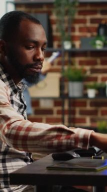 Dikey video: Afrikalı Amerikalı uzman gülümseyen ve grafik tabletle çalışan, yeni proje arayüzü geliştirmek için stilus kalem kullanan. Sanatsal zeka içeriği yaratan mutlu erkek işçi