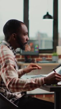 Dikey video: Tablet ve stil kalemle çalışan erkek grafik tasarımcısı rötuş yazılımında resimler düzenliyor. Renk derecelendirme ile rötuş çalışması yapan sanatçı editörü, fotoğrafçılık becerilerine sahip