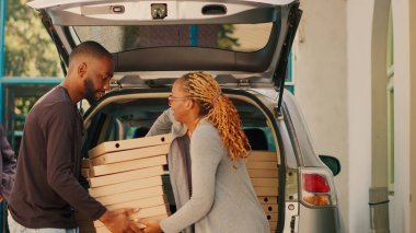 African american courier giving piles of pizza boxes to diverse people standing near building entrance. Food delivery employee delivering stacks of meal packages in car trunk. Tripod shot. clipart