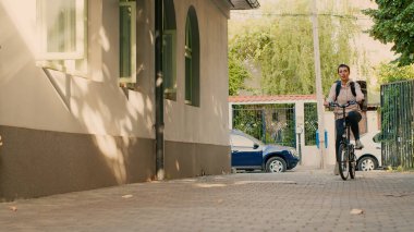 Yemek teslimatı kuryesi olarak çalışan bir kadın sokakta bisiklet sürüyor. Restoran yemeğini kapıya götürmek için termal sırt çantası taşıyor. Kadın taşıyıcı müşterilere fast food siparişi veriyor. El kamerasıyla..