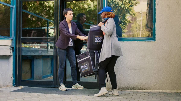 Pizzeria delivery worker delivering pizza box at front door, restaurant food delivery service. Young courier giving fastfood meal package to woman, carrying food backpack on street.