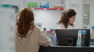 Afrikalı Amerikalı müşteriler eczaneden almak için eczacıya reçeteli ilaçları ilaç şişesinde soruyor. İlaç ürünleri ve ilaçlarla kadınlara hizmet eden bir tıp çalışanı..