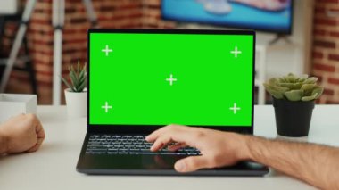 Masasında yeşil ekran şablonu olan dizüstü bilgisayarda çalışan genç yetişkin, boş krom anahtarı kontrol ediyor ve taşınabilir bilgisayardaki izole görüntüyü kontrol ediyor. Model kopyalama alanı ile bilgisayara bakıyorum. Tripod atışı. Kapat..