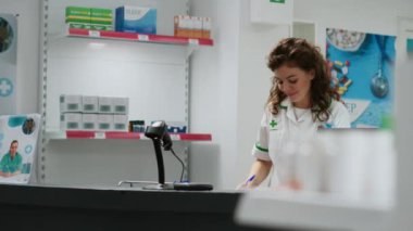Eczane tezgahında ilaç ve ilaç satan bir tıp çalışanı eczane masasında ilaç ve vitaminlerle çalışıyor. Müşterilere ilaç ve sağlık hizmetleri satın almalarında yardımcı olmak.