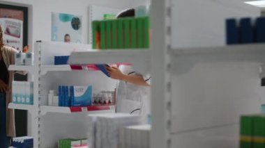 İlaç ve tedaviye yardımcı olmak için eczane raflarındaki destek kutularını inceleyen bir tıp çalışanı. Eczacılara bakıyor, notlar alıyor, eczanede çalışıyor..