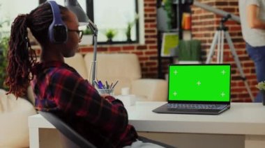 Kulaklık kullanan ve taşınabilir laptopta yeşil ekranla çalışan, kulaklıkla müzik dinleyen ve izole edilmiş kroma anahtar ekranını analiz eden serbest çalışan bir kadın. Boş model kopyalama alanı gösteriliyor.