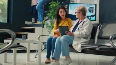 Sağlık merkezindeki kıdemli tıbbi danışman Asyalı hasta, tıbbi kontrol raporlarını analiz ediyor ve dijital tablet kullanıyor. Klinikte konsültasyonda hastalık teşhisi konan kişilerle konuşan bir doktor..