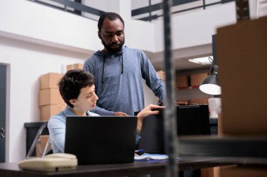 Depo teslimat ekibi depoda ambalaj üretiminde çalışırken metal kutucuk siparişlerini kontrol ediyor. Dizüstü bilgisayardaki sevkiyat lojistiğini analiz eden çok ırklı işçiler