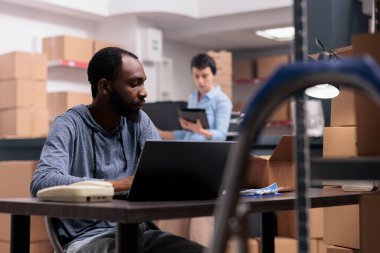 Çalışan müşteriye teslim etmeden önce kask kontrolü yapıyor, dizüstü bilgisayardaki müşteri sevkiyatlarını kontrol ediyor. Depoda çalışan teslimat departmanı müdürü.