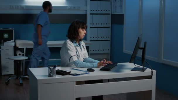 Lekarz Prowadzący Wpisując Wiedzę Medyczną Komputerze Sprawdzeniu Raportu Pacjenta Podczas — Wideo stockowe