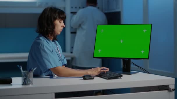 在检查预约期间 护士站在办公桌前看着有绿色屏幕模板的计算机 工作了好几个小时 在医院办公室输入医学知识的医生助理 — 图库视频影像