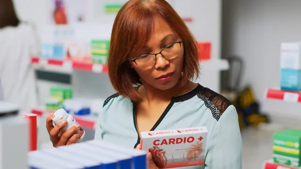 アジアの顧客は 医療小売店舗を訪問し 薬を購入する循環器系薬箱を見て 病気を治すために医薬品のパッケージや薬のボトルをチェック女性 手持ち撮影 — ストック写真