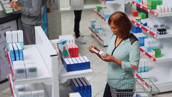 心脏有问题的妇女检查心脏科药丸盒 在药房寻求医疗保健治疗 亚洲人把疾病分析药品放在药店货架上 手持射击 — 图库照片