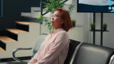 Asyalı bir kadın konsültasyon randevusunda doktorla görüşmek için bekliyor, sağlık hizmeti almak ve hastalıkları tedavi etmek için check-up ziyareti yapıyor. Hasta klinik lobisinde oturuyor..