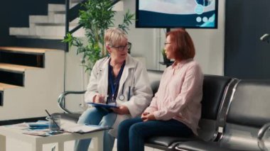 Yaşlı doktor ve Asyalı hasta bekleme salonunda sağlık danışmanlığı yapıyor, uzman doktorla randevuları var. Tekerlekli sandalye kullanıcısı ve lobideki insanlarla konuşan bir doktor..