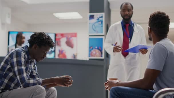 全科医生带病人去会诊 年轻人坐在保健中心大堂 病人与医生会诊治病 并接受治疗 手持射击 — 图库视频影像