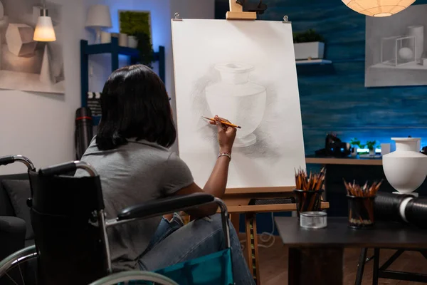 年轻有才华的女性患有慢性变性疾病 在家里画铅笔很方便 非裔美国女性素描艺术家在画架上创作壶的素描作品 — 图库照片