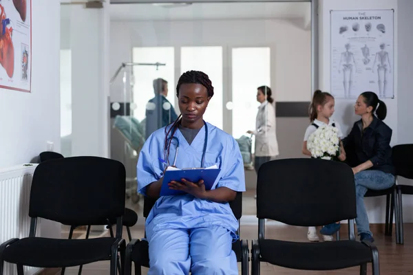 Αφροαμερικανή Νοσοκόμα Συμπληρώνει Χαρτιά Των Ασθενών Που Κάθονται Στις Καρέκλες — Φωτογραφία Αρχείου