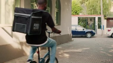Bisiklete binen Afrikalı Amerikalı teslimatçı ve yemek siparişini sırt çantasıyla getiren, müşterilere yemek dağıtan. Paket teslimatı için paket paket servis eden restoran kuryesi..