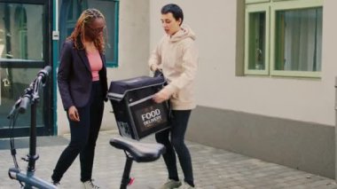 Paket servis çalışanı. Girişte bekleyen müşteriye fast food siparişi veriyor. Restoran paketi veriyor. Kadın teslimatçı elinde öğle yemeği çantasıyla, bisikletli kadın..