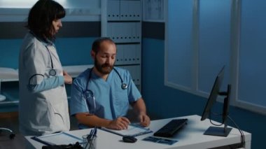 Hasta hastalıkları raporuna bakan doktor ve asistan sağlık tedavisi planlama semptomlarını tartışıyor. Hastane ofisinde gece vardiyasında çalışan tıbbi personel. Tıp konsepti