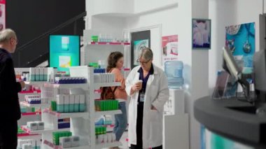Yaşlı eczacı kahve fincanı içiyor ve vitamin kutularıyla eczane raflarını kontrol ediyor. Eczanedeki paketlerdeki ilaç ve takviyeleri analiz eden bir sağlık uzmanı..