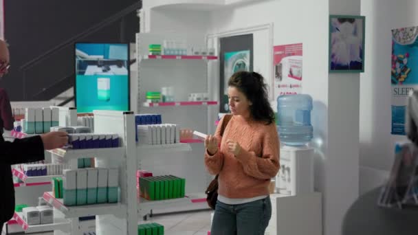 若い女性は 処方治療のためにビタミンや薬の箱を購入し 棚に医療リーフレットを読んでいます 薬やサプリメント 医薬品をチェックする女性のクライアント — ストック動画