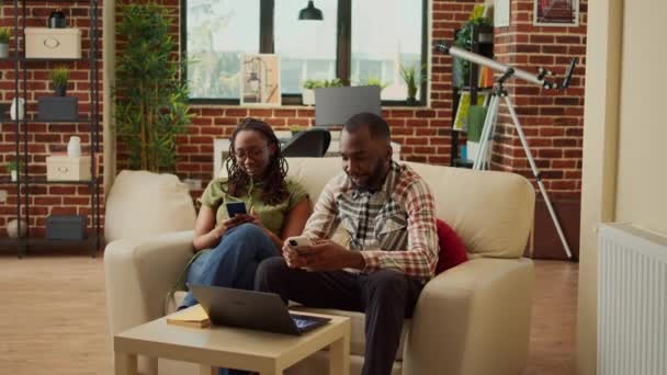 快乐的人们舒适地坐在家里 在手机上浏览社交媒体应用程序 放松身心 男朋友和女朋友用智能手机舒服地睡在沙发上 — 图库视频影像