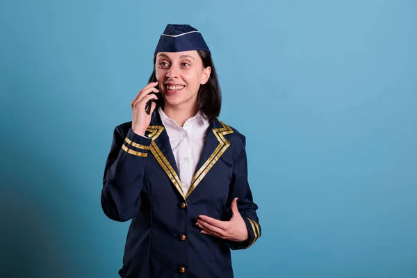 stock image Smiling cheerful flight attendant talking on smartphone, holding mobile phone, having conversation. Happy stewardess in uniform answering telephone call, air hostess standing