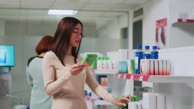 Eczanede ilaç broşürleri okuyan, sağlık ürünleri satın almak için ilaçları kontrol eden bir kadın müşteri. Müşteri reçeteli tedavi veya ilaç almak için ilaç kutularına bakıyor.