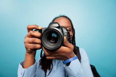 Amateur photographer taking photos with modern DSLR device while standing on blue background. Photography entusiast enjoying taking pictures with photo camera. Studio shot clipart