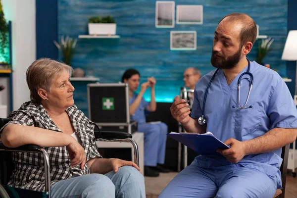 Чоловіча Медсестра Яка Пояснює Лікування Пацієнтки Старшого Віку Робить Нотатки — стокове фото