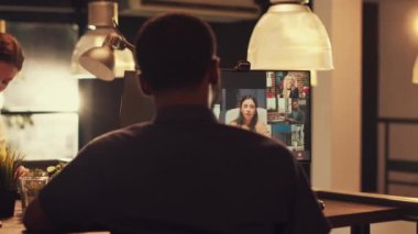 Ofis çalışanı, gün batımında web kamerasıyla bilgisayardaki video görüşme toplantısına katılıyor. İnternetteki telekonferans görüşmesinde insanlarla konuşuyor. Uzak internet video konferansı, telekomünikasyon ile çalışmak.